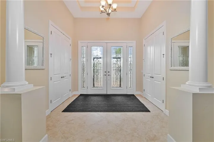 Foyer featuring ornate columns, light tile patterned floors, a chandelier, and french doors