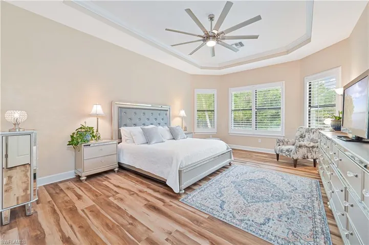 Bedroom featuring a raised ceiling, light wood-style floors, a ceiling fan, and crown molding
