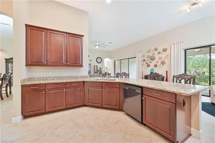 Kitchen with arched walkways, light stone counters, a peninsula, dishwasher, and light tile patterned flooring