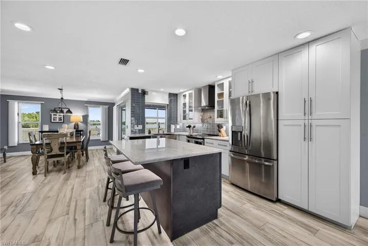 Two tone kitchen with stainless steel appliances, light stone counters, glass fronted cabinets, a center island, and tasteful backsplash
