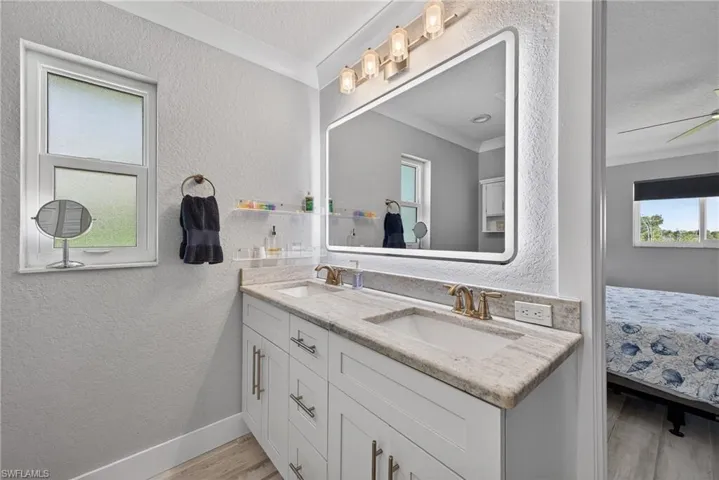 Ensuite bathroom featuring a textured wall, double vanity, light wood finished floors, ornamental molding, and a textured ceiling