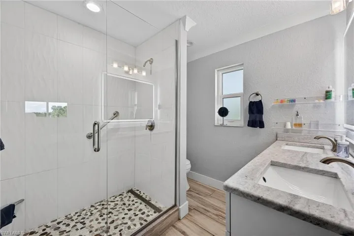 Full bath featuring a textured wall, double vanity, a shower stall, a textured ceiling, and light wood finished floors