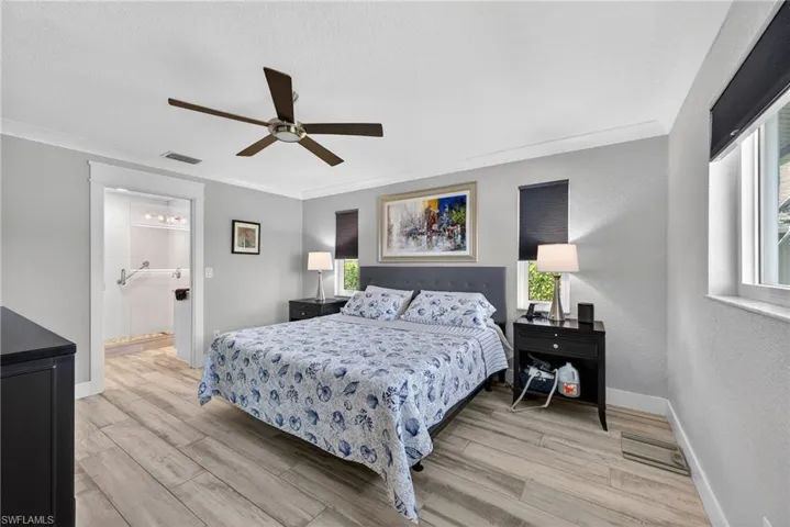 Bedroom featuring light wood-style floors, a ceiling fan, a textured wall, ensuite bathroom, and ornamental molding