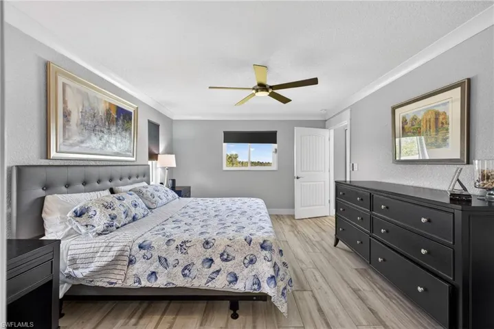 Bedroom with light wood-style floors, a textured wall, a ceiling fan, ornamental molding, and a textured ceiling