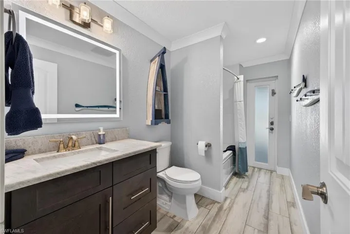 Bathroom featuring a textured wall, a shower with shower curtain, vanity, light wood finished floors, and ornamental molding