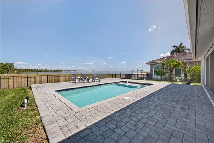 View of swimming pool with a water view, patio surround, and a fenced backyard