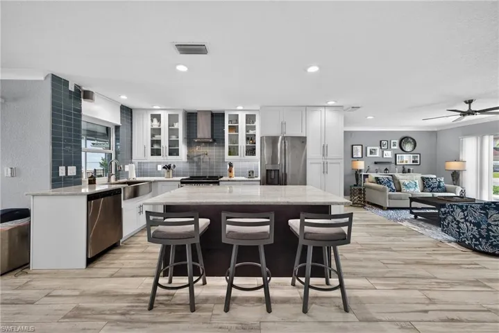 Kitchen with plenty of natural light, light stone counters, a kitchen breakfast bar, glass fronted cabinets, and ornamental molding
