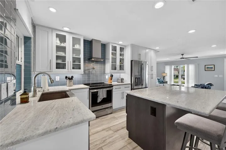 Kitchen with light stone countertops, stainless steel appliances, a center island, a breakfast bar area, and light wood-style flooring
