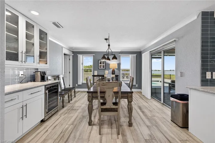Dining room featuring a textured wall, wine cooler, a textured ceiling, ornamental molding, and light wood-style flooring