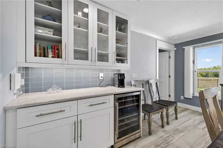 Bar with white cabinets, beverage cooler, glass insert cabinets, light wood-style floors, and a textured ceiling