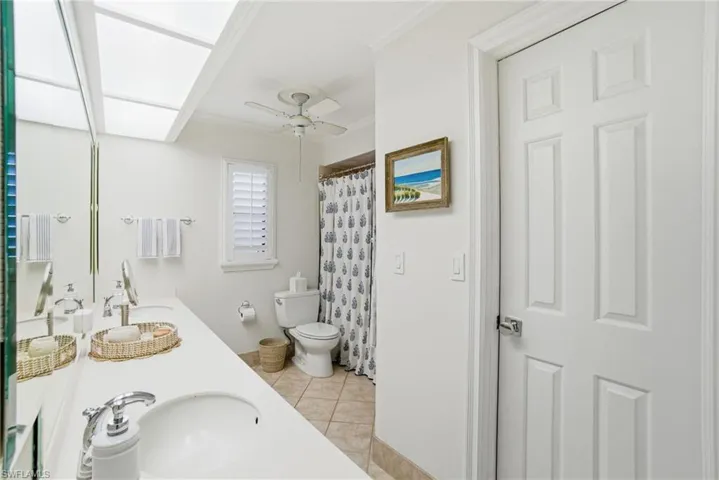 Bathroom featuring double vanity, a shower with curtain, light tile patterned floors, and a ceiling fan