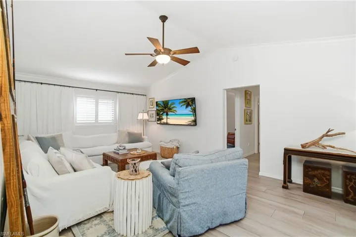 Living area featuring light wood finished floors, lofted ceiling, crown molding, and a ceiling fan