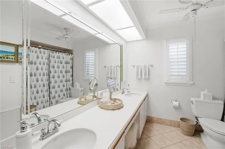 Full bath with ceiling fan, double vanity, a shower with shower curtain, crown molding, and light tile patterned flooring