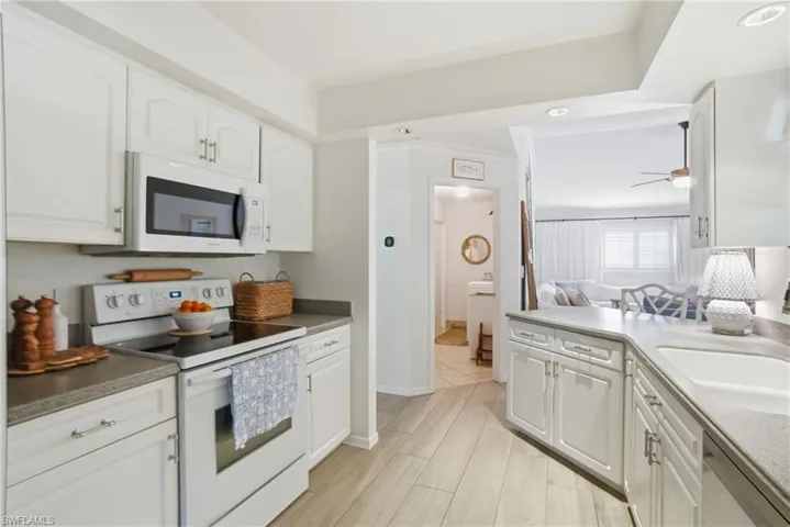 Kitchen featuring white appliances, white cabinets, wood finish floors, open floor plan, and a ceiling fan