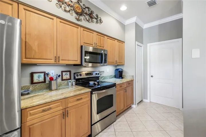 Kitchen featuring appliances with stainless steel finishes, crown molding, light stone countertops, light tile patterned flooring, and brown cabinets