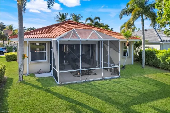 Rear view of property with a tiled roof, a lanai, and a yard