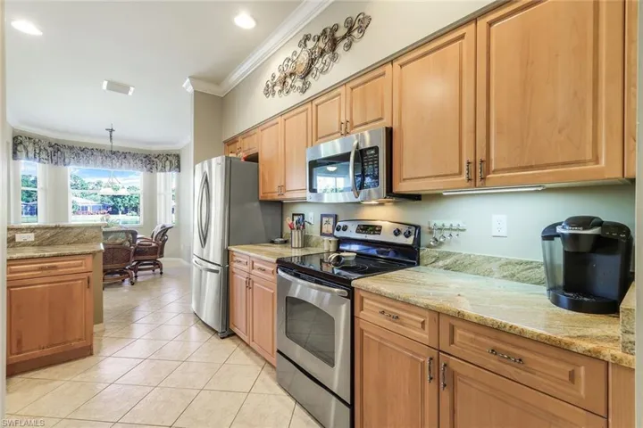 Kitchen featuring appliances with stainless steel finishes, ornamental molding, light tile patterned floors, hanging light fixtures, and light stone counters