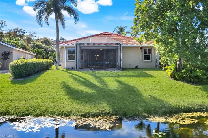 Back of house with a water view, a lanai, and a lawn