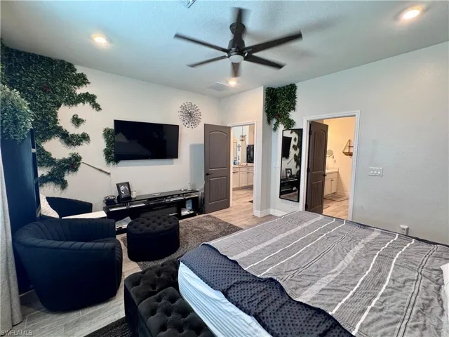 Bedroom featuring a textured ceiling, light wood-style floors, ensuite bath, visible vents, and a ceiling fan
