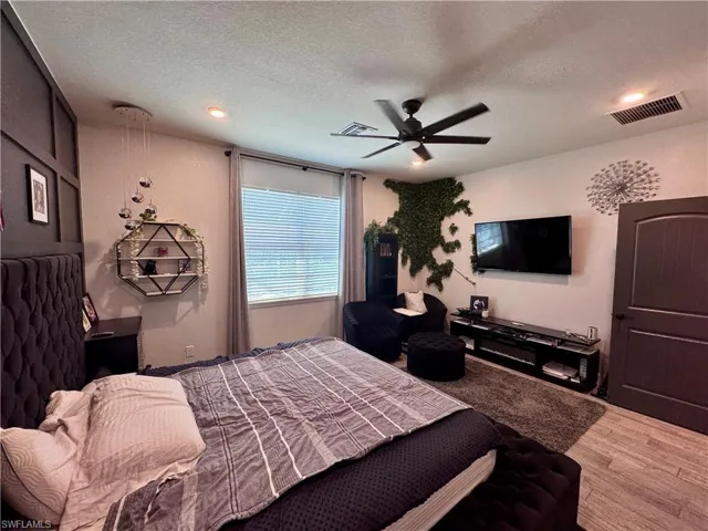 Bedroom with a textured ceiling, visible vents, a ceiling fan, and wood finished floors