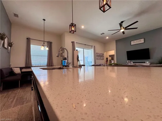 Kitchen featuring a sink, a ceiling fan, light stone countertops, hanging light fixtures, and visible vents