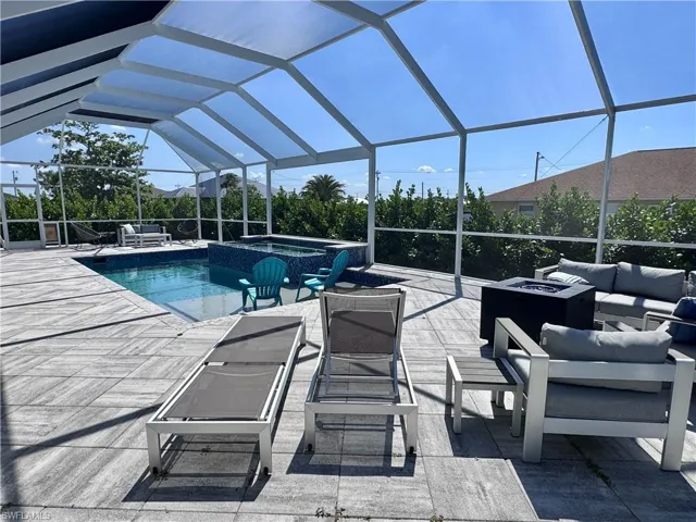 View of swimming pool with glass enclosure, a pool with connected hot tub, a patio area, and an outdoor living space with a fire pit