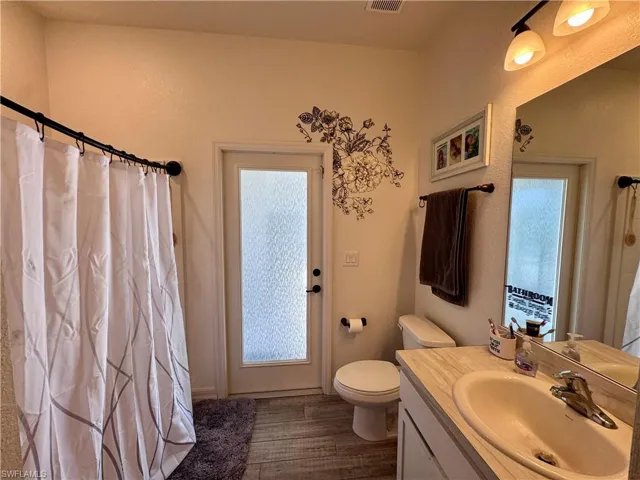 Bathroom featuring vanity, toilet, visible vents, curtained shower, and wood finished floors