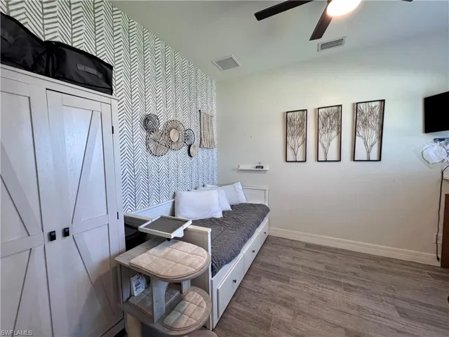 Bedroom with baseboards, visible vents, wood finished floors, and an accent wall