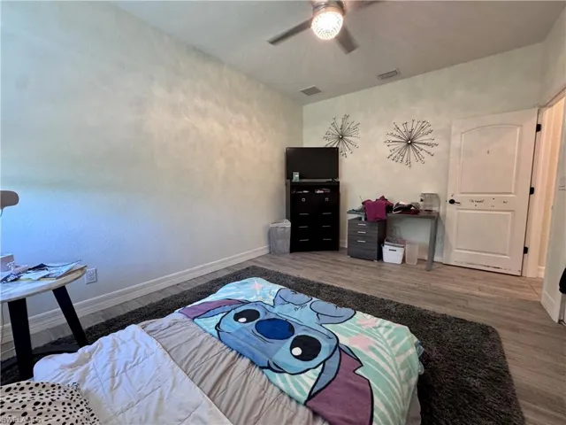 Bedroom featuring a ceiling fan, visible vents, baseboards, and wood finished floors