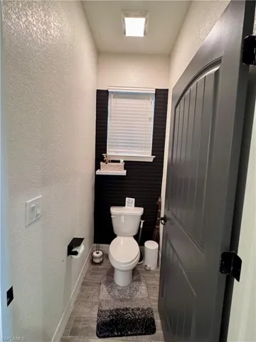 Bathroom with toilet, a textured wall, and baseboards