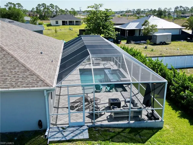 Rear view of property featuring a swimming pool, glass enclosure, a shingled roof, a yard, and a patio area