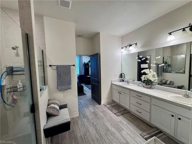 Bathroom featuring visible vents, a shower stall, double vanity, wood finish floors, and a sink
