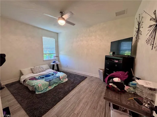 Bedroom with baseboards, visible vents, wood finished floors, and a ceiling fan