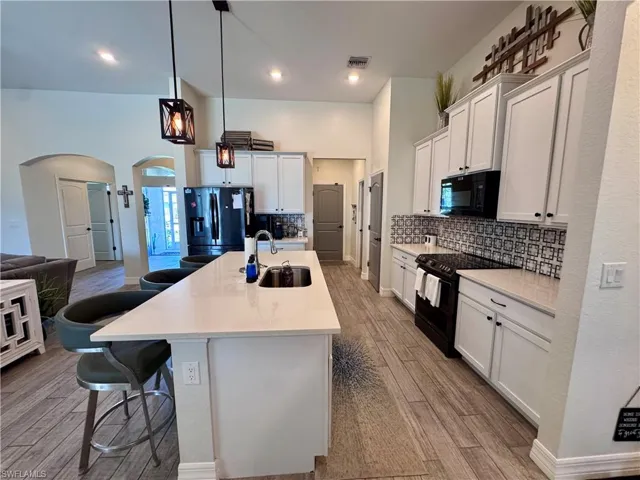 Kitchen with a kitchen bar, a sink, arched walkways, visible vents, and black appliances
