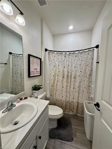Full bathroom featuring vanity, toilet, a shower with shower curtain, visible vents, and wood finished floors
