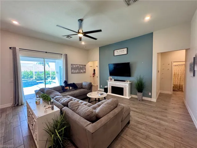 Living area with a fireplace, wood finished floors, baseboards, visible vents, and ceiling fan