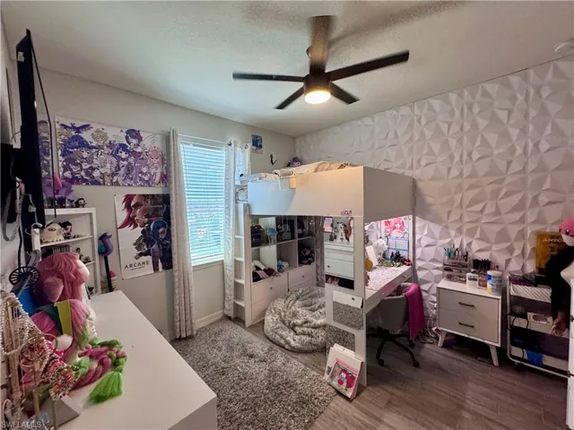 Bedroom featuring a ceiling fan, wood finished floors, a textured ceiling, baseboards, and wallpapered walls