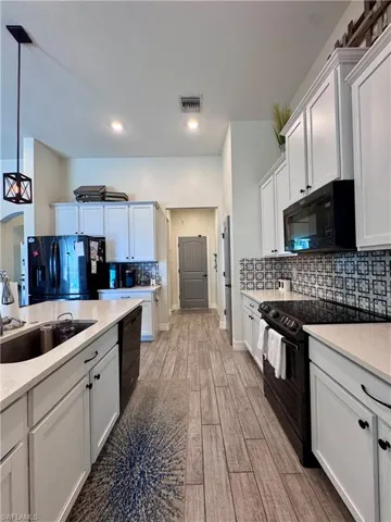 Kitchen featuring light countertops, visible vents, a sink, light wood-type flooring, and black appliances