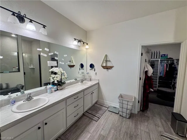 Bathroom with double vanity, a sink, tiled shower, and wood finished floors