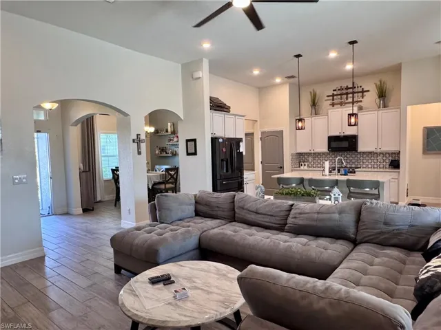 Living room featuring baseboards, wood finished floors, a ceiling fan, arched walkways, and a high ceiling