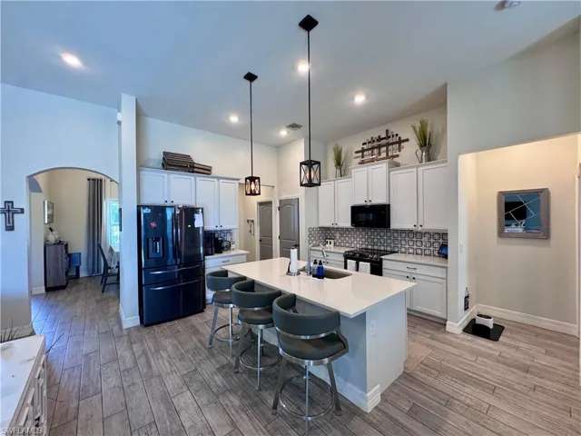 Kitchen featuring backsplash, a high ceiling, a sink, arched walkways, and black appliances
