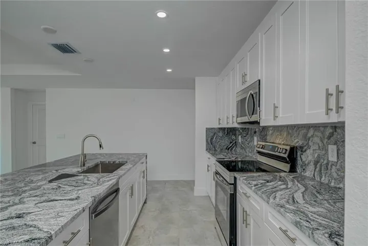 Kitchen featuring stainless steel appliances, light stone counters, white cabinetry, and recessed lighting