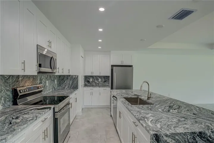 Kitchen featuring stainless steel appliances, light stone counters, recessed lighting, a center island with sink, and white cabinets