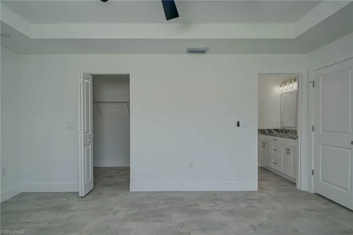 Unfurnished bedroom featuring a walk in closet, a ceiling fan, a tray ceiling, and connected bathroom