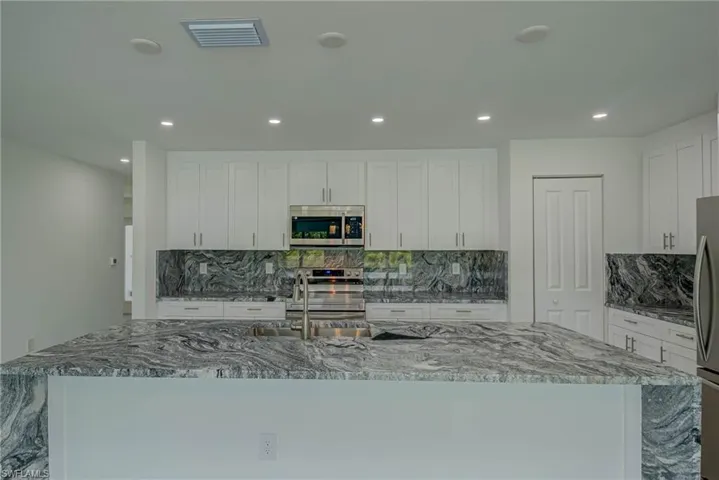 Kitchen with light stone counters, tasteful backsplash, a center island with sink, white cabinetry, and recessed lighting
