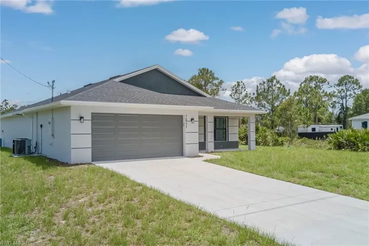 Ranch-style house with an attached garage, a front yard, driveway, stucco siding, and roof with shingles