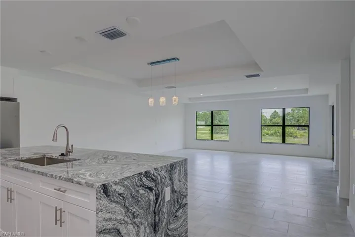 Kitchen featuring a tray ceiling, white cabinets, light stone counters, open floor plan, and decorative light fixtures