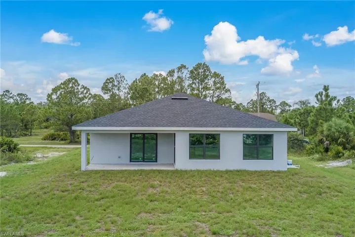 Back of property with stucco siding, a lawn, a patio, and roof with shingles