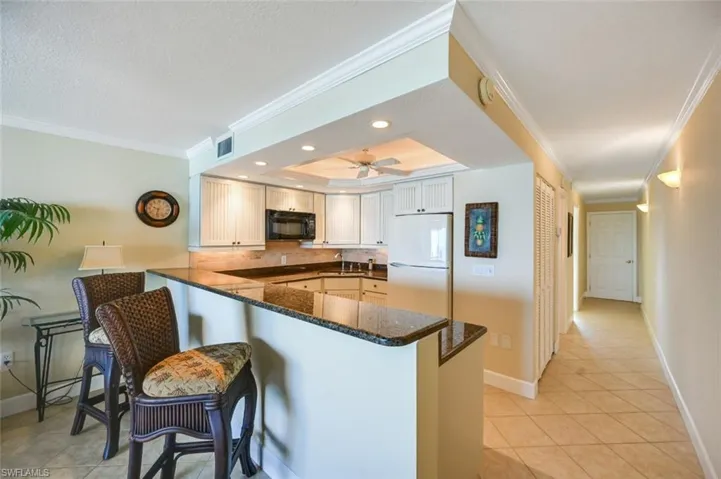 Kitchen featuring white fridge, dark stone counters, kitchen peninsula, and ceiling fan