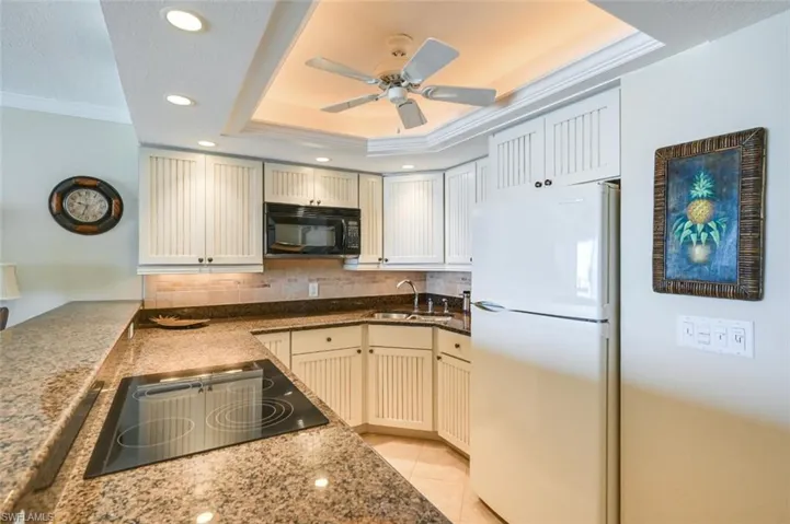 Kitchen featuring a raised ceiling, black appliances, sink, decorative backsplash, and ceiling fan
